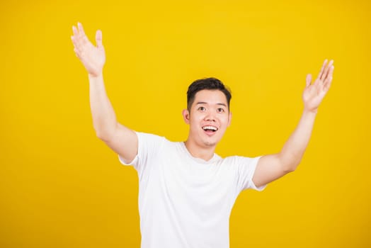 Asian handsome young man smile positive shaking hands enthusiastic shouting yes for win competition, male raising his fists Yes! with smiling delighted face, studio shot isolated on yellow background