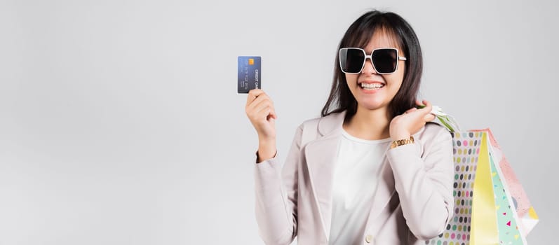 Woman with glasses confident shopper smile hold online shopping bags and credit card for payment on hand, Portrait excited happy Asian female fashion shop studio shot isolated on white background