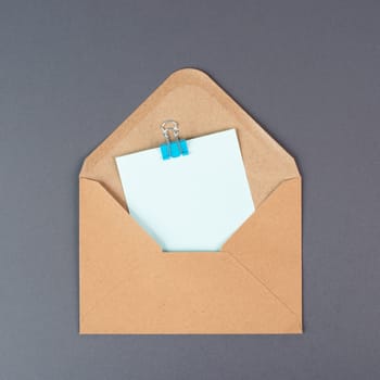 Envelope with an empty paper on a gray colored background, copy space for text, greeting card, communication and announcement concept, reminder