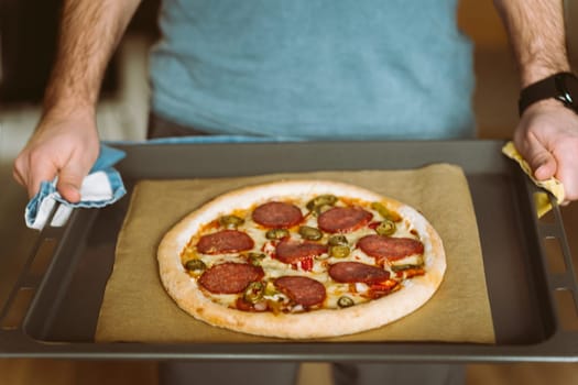 A man holds a baking sheet with pizza. Baking sheet covered with baking paper.