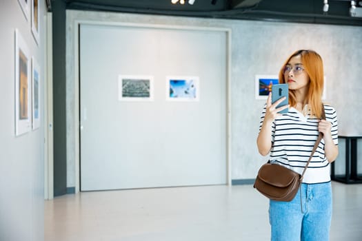 Visitor woman standing takes picture art gallery collection in front framed paintings pictures on white wall with mobile phone, people watch at photo frame with smartphone at artwork gallery show