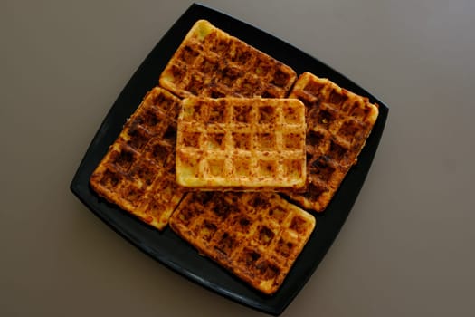 Sweet waffles prepared for serving. A tasty dessert eaten with fruit and preserves. Dark background