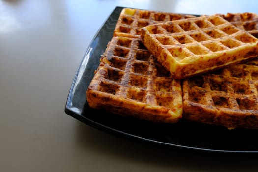 Sweet waffles prepared for serving. A tasty dessert eaten with fruit and preserves. Dark background