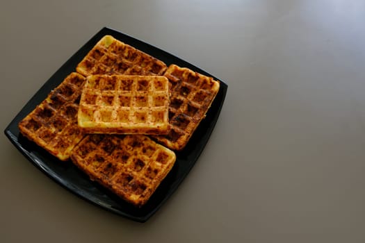 Sweet waffles prepared for serving. A tasty dessert eaten with fruit and preserves. Dark background