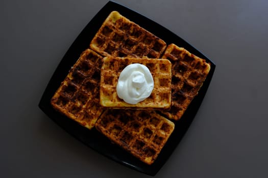 Belgian waffles on a black plate, on the biege table and souse it in sour cream