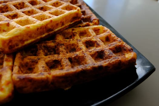 Sweet waffles prepared for serving. A tasty dessert eaten with fruit and preserves. Dark background