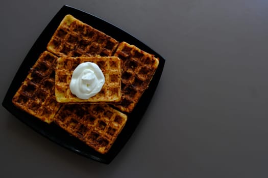 Belgian waffles on a black plate, on the biege table and souse it in sour cream