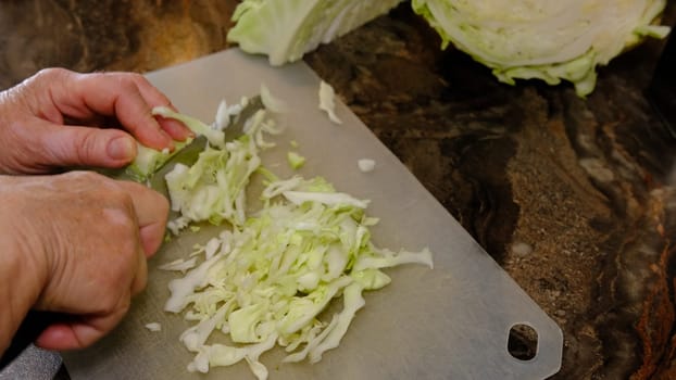 old women's hands with a knife cut cabbage on the cutting Board.