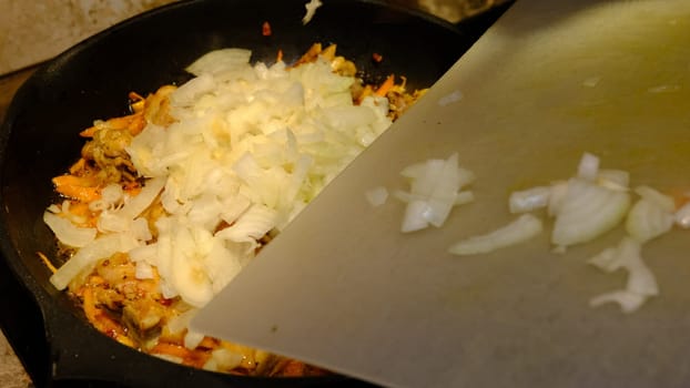 Homemade Korean Spicy chiken dish, frying chiken with carrot in a pan with sunflower oil. Add onion.
