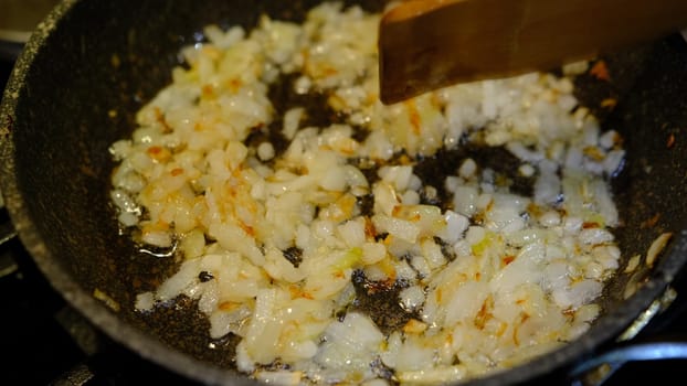 cooking and mixing fried onions by wooden spoon in a pan with sunflower oil.