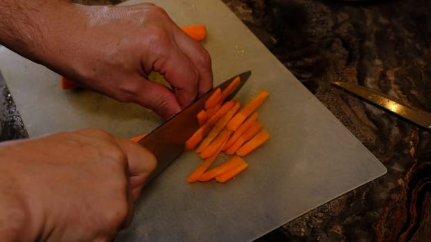 Handsof man in kitchen cutting carrot with knife.