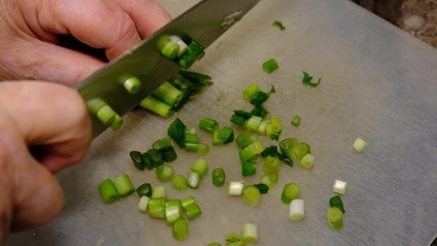 old woman hands cutting young onion on the kitchen.