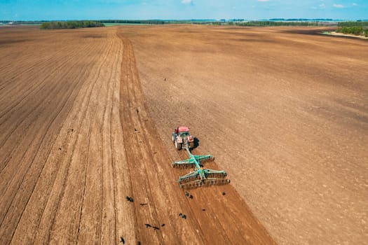 Aerial View. Tractor Plowing Field In Spring Season. Beginning Of Agricultural Spring Season. Cultivator Pulled By A Tractor In Countryside Rural Field Landscape.