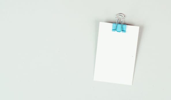Blank white paper with a paperclip on a gray colored background, copy space for text, reminder or message in the office, communication concept