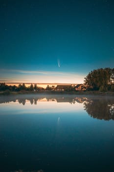 Dobrush, Belarus. Comet Neowise C2020f3 In Night Starry Sky Reflected In Small Lake Waters