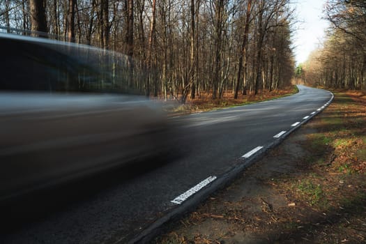 A car driving fast on a road through the forest, autumn day