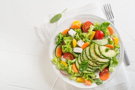 Healthy green salad with avocado, feta cheese and fresh vegetables on white background close up