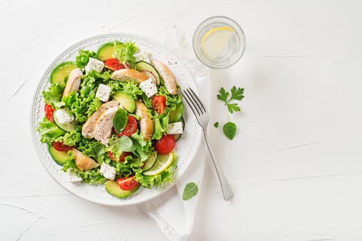Fresh green salad with chicken breast, feta cheese and tomato on white table background