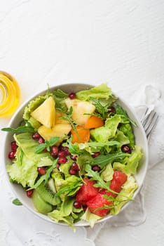 Fresh salad with fruits and greens on white table background top view with space for text. Healthy food.