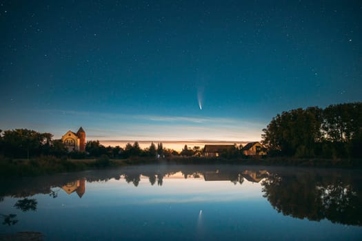 Dobrush, Belarus. Comet Neowise C2020f3 In Night Starry Sky Reflected In Small Lake Waters