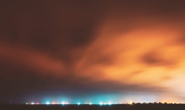 Night Sky With Rare Glowing Stars Shining Through The Cloudiness Overcast Above Countryside Town Landscape. Rural Field Meadow In Early Spring.