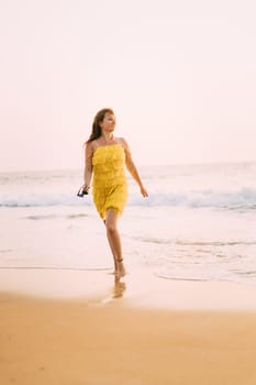 Goa, India. Young Caucasian Woman In Yellow Dress Walking On Seashore And Enjoying Life In Summer Sunlight.
