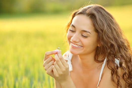 Happy woman looking at engagement ring sitting in a wheat field