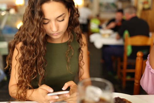 Distracted woman using cell phone sitting in a restaurant