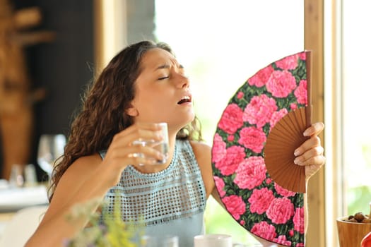 Stressed woman getting hot and fanning suffering heat stroke in a restaurant