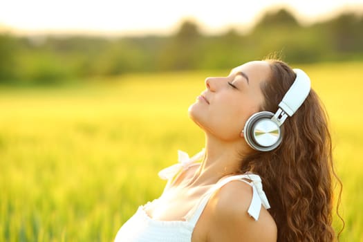 Side view portrait of a woman meditating listening music with headphones in a wheat field