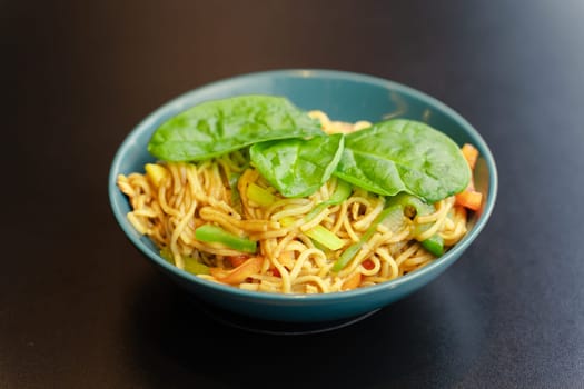 Spaghetti with vegetables and basil leaves in a turquoise plate, a kind of closeness