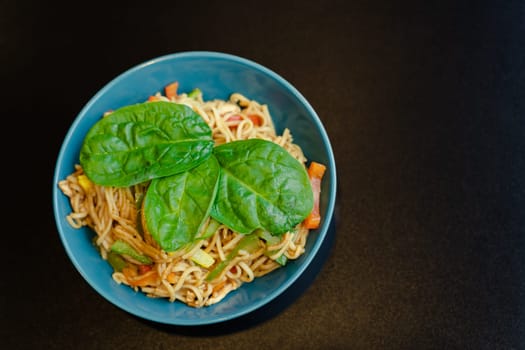 Top view of a plate of spaghetti with vegetables and basil leaves.
