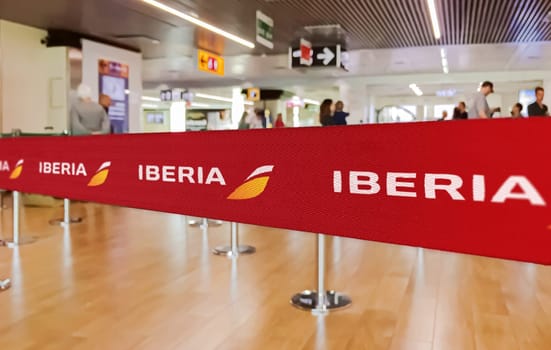Madrid, Spain, July 2022: Red belt barrier with white Iberia airlines logo. Iberia is the Spanish flag carrier. Travel and airport security