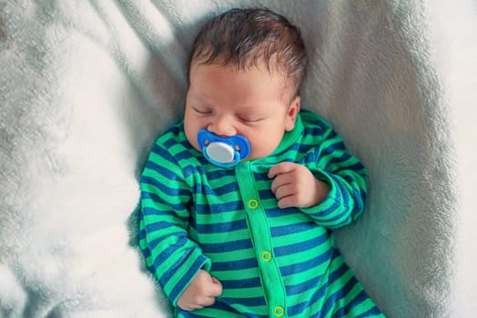 portrait of a newborn baby boy who sleeps with a pacifier in his mouth
