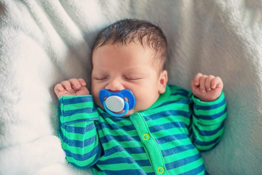 Sleeping newborn baby with raised arms and a pacifier in his mouth