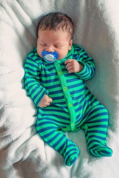 newborn baby sleeping on a white blanket with a pacifier in his mouth