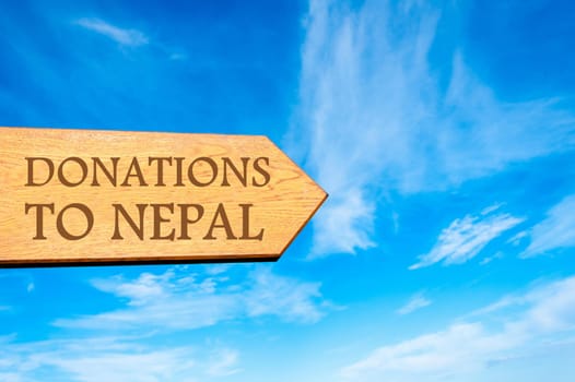 Wooden arrow sign with message DONATIONS TO NEPAL against clear blue sky with copy space available. Travel destination conceptual image