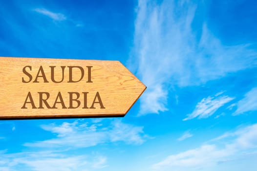 Wooden arrow sign pointing destination SAUDI ARABIA against clear blue sky with copy space available. Travel destination conceptual image