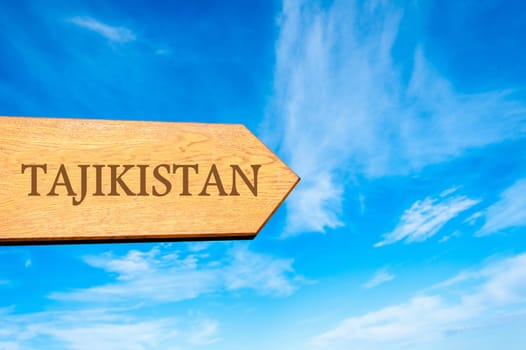 Wooden arrow sign pointing destination TAJIKISTAN against clear blue sky with copy space available. Travel destination conceptual image