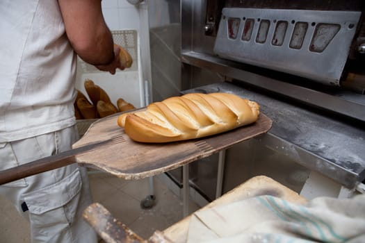 Baker taking fresh baked bread from oven. Manufacturing process of spanish bread