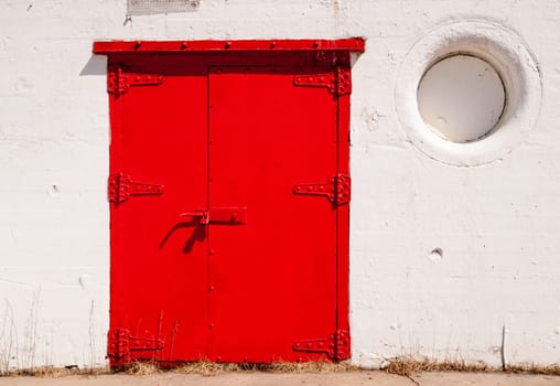 Stark composition contrast between red door and white walls at lighthouse base