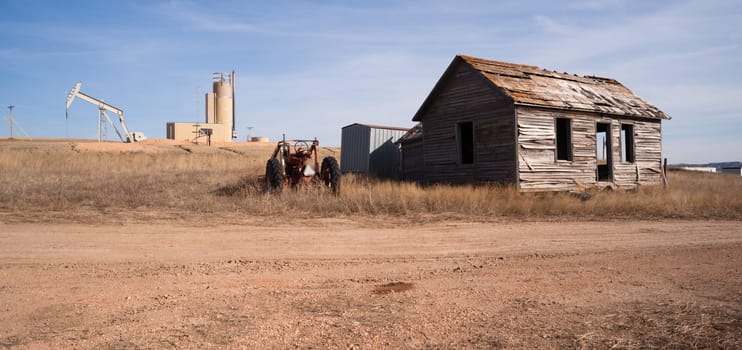 An abandoned tractor and cabin sit in the foreground of a fracking oil pump jack