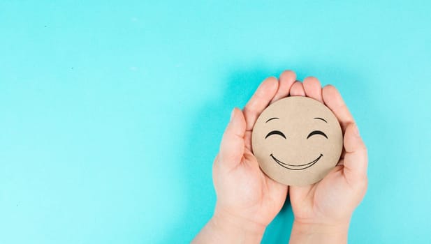 Holding a smiling face in the hands, mental health concept, positive mindset, support and evaluation symbol