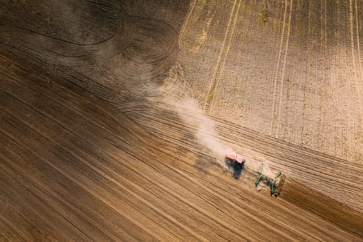 Aerial View. Tractor Plowing Field. Beginning Of Agricultural Spring Season. Cultivator Pulled By A Tractor In Countryside Rural Field Landscape. Dust Rises From Under Plows.