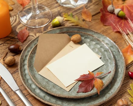 Autumn rustic table setting with blank place card and envelope between colorful leaves and berries close up, mockup. Flat lay Horizontal card on wooden table, flat lay, copy space. Thanksgiving or harvest