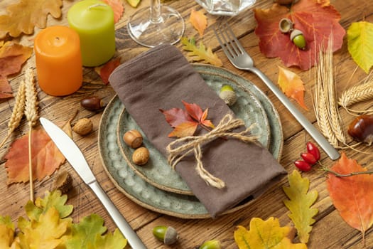 Autumn rustic table setting between leaves and berries on vintage wooden table close up. Thanksgiving, halloween or harvest concept