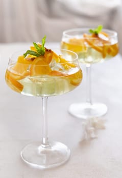 Transparent cocktail with ice cubes in a champagne coupe glass decorated with slices of orange close up. Tropical drink at the bar. Summer vacation mood