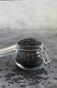Glass jar of dry black lentils beans on grey table close up. Healthy eating, protein source for vegan and vegetarian diet. Traditional Asian and North African cuisines ingredient