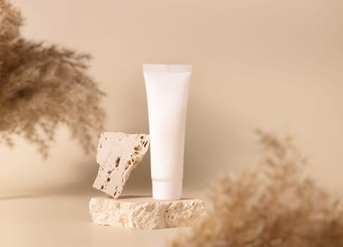 White plastic cream tube on travertine stone near dry pampas grass on light yellow, close up, mockup. Skincare beauty product. Natural cosmetics. Boho composition..