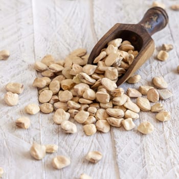 Scoop of raw dry Grass pea close up on wood. Healthy, protein source for vegan and vegetarian diet. Traditional Italian apulian cuisine ingredient. Legumes known as Cicerchia, Vetch, Blue Sweet Pea